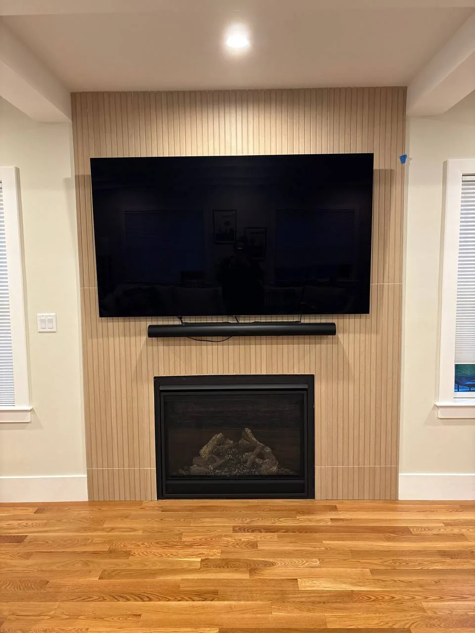 A large TV and a soundbar mounted on a slatted wood accent wall directly above a built-in gas fireplace in a Riverview-area home.