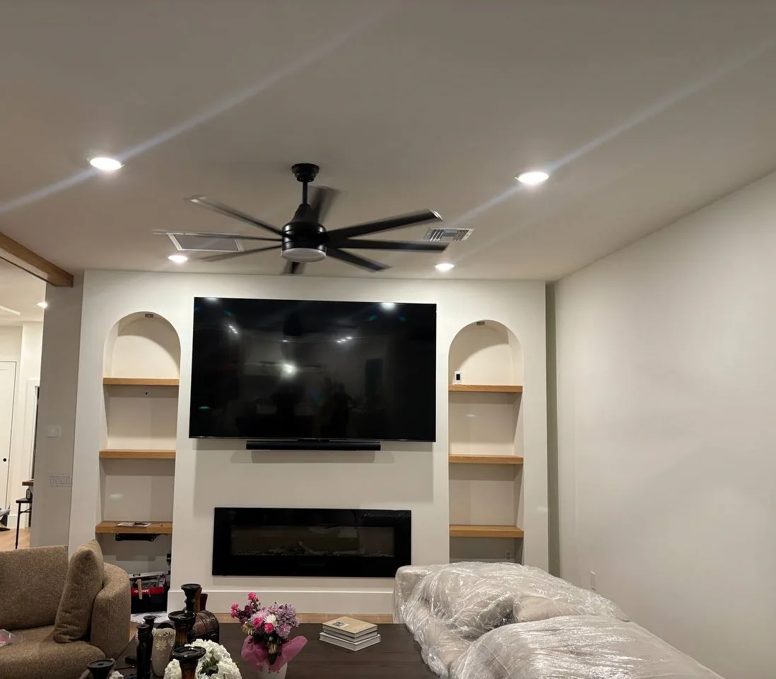 A large TV and soundbar mounted between two arched built-in shelving alcoves, above a linear electric fireplace in a bright living room.